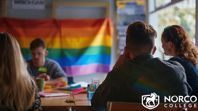 A team meeting in progress with a rainbow flag visible in the background, symbolizing LGBTQ+ inclusivity in the workplace.