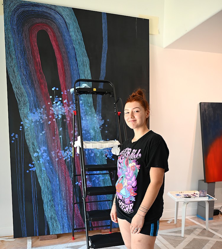 NC alumna Natalie Nicole stands with one of five large-scale paintings she assisted with