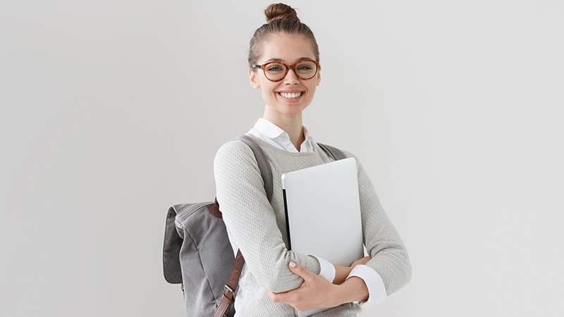 Female student wearing glasses and backpack and holding laptop